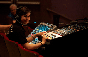 Intern Photo of an intern sewing at a table with a large 2-tiered rack of costumes behind them.