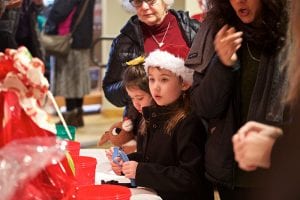 Photo from the event of children holding strings of blue tickets with their parents right behind them. The kids look on curiously.