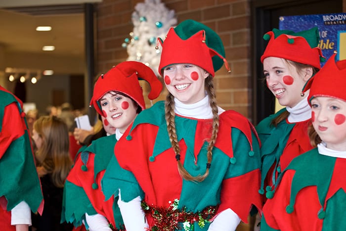 Photo from the event of "Elves" in red and green costumes, several of them lined up in a row smiling for the cameras.