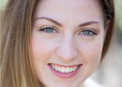 A smiling young woman with green eyes and light brown hair.