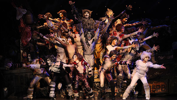 Old theatre - exterior - night Photo of the 2011 production of Cats. The entire cast of over 20 performers is in a group formation, reaching their arms out toward the audience.