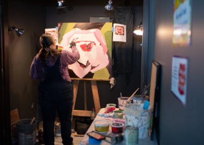 Photo from the Gala of a young woman painting an abstract and colorful painting on a roughly 24 inch by 24 inch canvas.