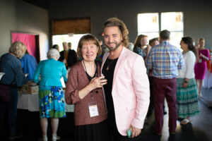Photo from the Gala of two attendees, a man and woman, holding each other side by side and smiling for the camera in the new crowded rehearsal hall.