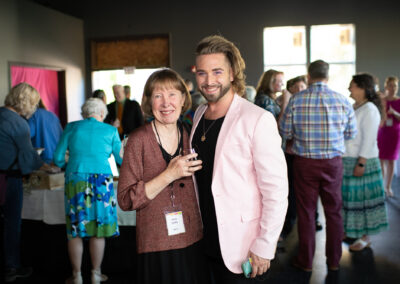 Photo from the Gala of two attendees, a man and woman, holding each other side by side and smiling for the camera in the new crowded rehearsal hall.