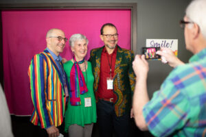 Photo from the Gala of a man using a smart phone to take a photo of three other brightly dressed attendees.