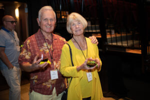 Photo from the Gala of a man and woman, side by side, his arm around her shoulder. He is wearing a deep red Hawaiian shirt and she is wearing a bright yellow shirt and sweater.