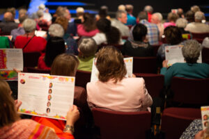 Photo from the Gala, taken from behind, of the crowd seated in the theatre reading their programs and chatting.