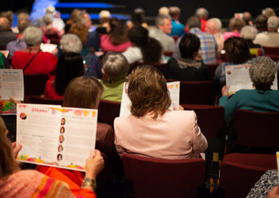 Photo from the Gala, taken from behind, of the crowd seated in the theatre reading their programs and chatting.