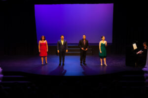 Photo from the Gala of four performers on stage, (from left to right) of a woman, two men, and another woman, all elegantly dressed and singing.