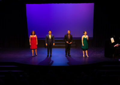 Photo from the Gala of four performers on stage, (from left to right) of a woman, two men, and another woman, all elegantly dressed and singing.