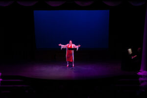 Photo from the Gala of a woman on stage singing in a bold red dress and a sheer floral-printed robe on top.
