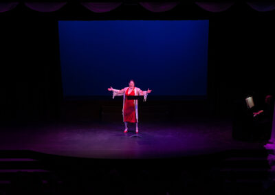 Photo from the Gala of a woman on stage singing in a bold red dress and a sheer floral-printed robe on top.