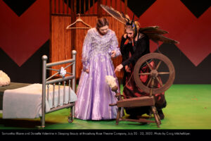 Photo of Samantha Blaine as Princess Penelope (Sleeping Beauty) and Danielle Valentine as Isadore the Witch. Harriet shows Penelope the cursed spinning wheel to trick her into pricking her finger.