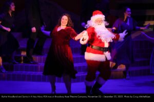 Blythe Woodland and Santa in "A Very Merry PDX-mas" at Broadway Rose Theatre Company, November 23 - December 22, 2022. Photo by Craig Mitchelldyer.