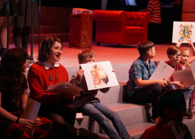 Kids sitting on the front of the stage participate in The 12 Days of Christmas, holding up signs to prompt the next lyrics.