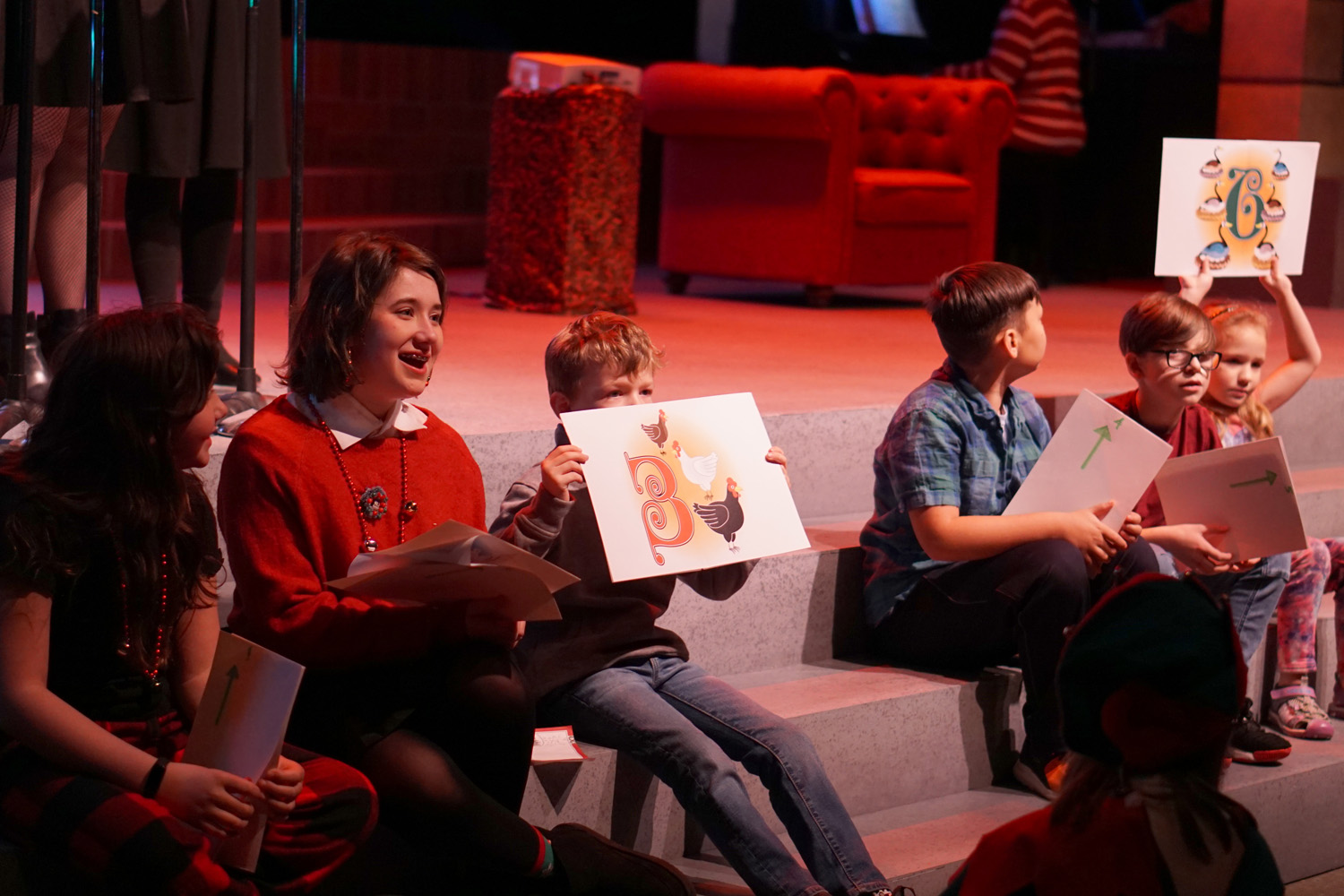 Kids sitting on the front of the stage participate in The 12 Days of Christmas, holding up signs to prompt the next lyrics.