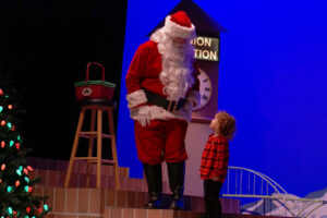 Santa standing next to a child looking up at him in wonder.