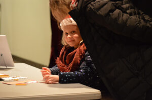 The girl writing down her Christmas list for Santa looking up at the camera.
