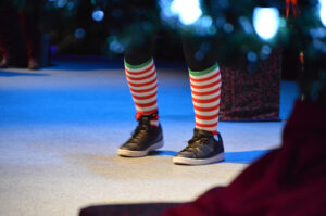 A pair of candy-striped socks and high-top sneakers showing beneath a Christmas tree.