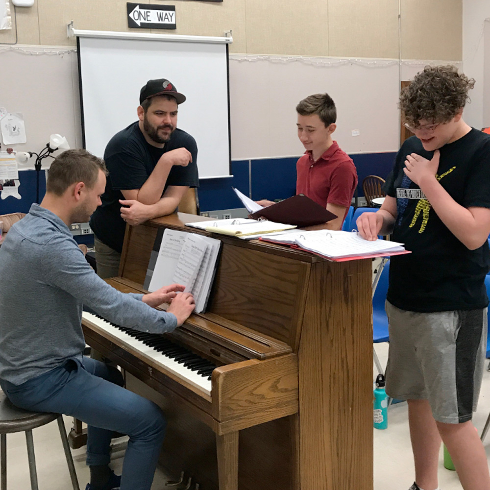 Education in Summer 1 Teen Summer Production performers rehearsing around a piano for Tuck Everlasting - 2019.