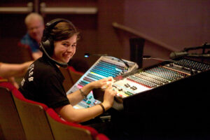 Photo of a sound operation intern at the sound board smiling toward the camera.
