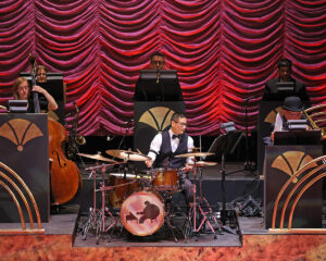 The band for Ain't Misbehavin' in the bandstand on stage with a vivid red-lit curtain behind them.