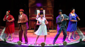 Production photo from Ain't Misbehavin', showing the whole cast across the stage, dancing in unisons around the upstage piano.