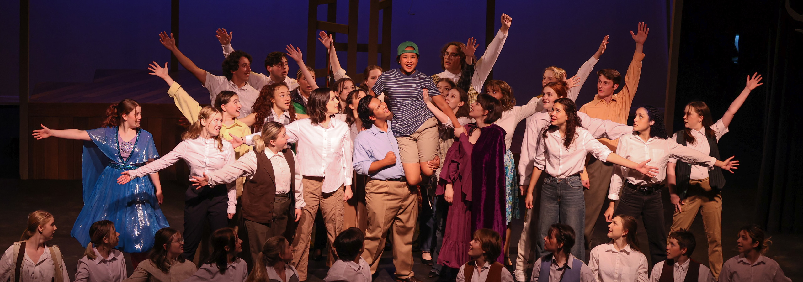 Photo from our production of Big Fish, showing the end of the song "Be the Hero". The entire cast surrounds a young Will Bloom and lifts him over their shoulders triumphantly.