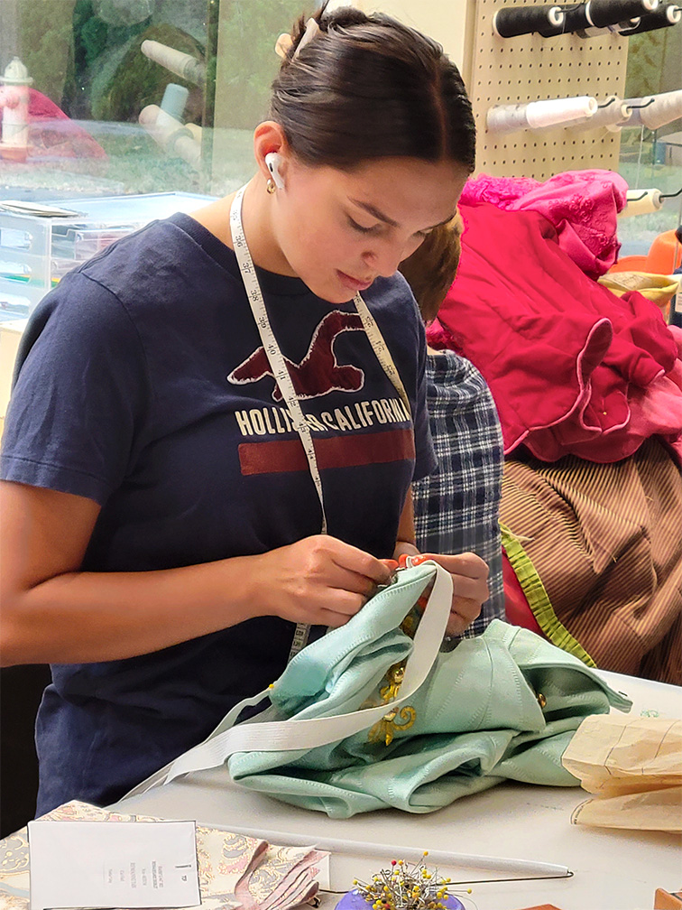 Photo of a costume shop intern at a table focusing on hand stitching.