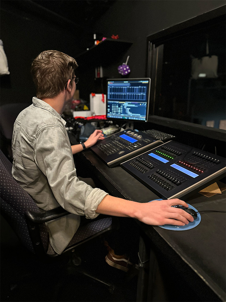 Photo of a light board operator intern in the booth setting the lighting cues.