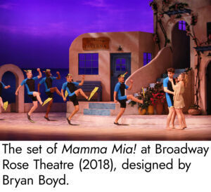 Photo of the set of Mamma Mia, the floor painted to be a sandy beach complete with ripples in the sand to show where the ocean's waves ebb and flow. The buildings up stage are distinctly mediterranean, with a stucco clay look and covered with climbing ivy.