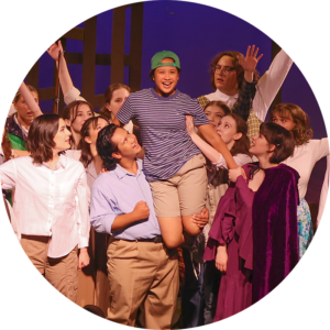 Photo from our 2023 Teen Production of Big Fish. Photo of the end of the song "Be the Hero" where the whole cast has lifted Will up on their shoulders, encouraging him to be the hero of his own story.