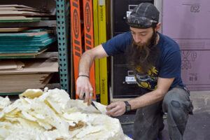 Photo of Alex Agnes-Cordry hard at work, sculpting a tree stump out of wood and foam.