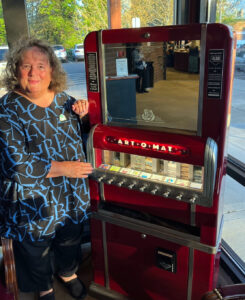 Photo of Karen Van Hatcher standing next to the Art-o-mat machine, her wonderful contribution to the Broadway Rose lobby.