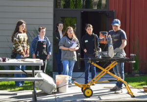 Photo of interns at orientation around a chop saw with our facilities manager and staff carpenter Mitchell Dummer.