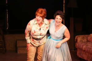 Photo of Sharon Maroney as Louise Seger and Sara Catherine Holder as Patsy Cline, hugging each other with one arm and looking out to the audience, smiling and laughing.