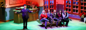 Photo of the cast of Home for the Holidays singing out to the audience from the bus station bench.