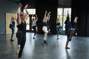 Photo from a Broadway Rose dance class showing our adult students during a short dance routine, their arms in the air and their right legs kicked up high.