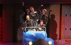 Photo from our 2015 production of Grease showing the boys in a small blue hotrod singing Greased Lightning.