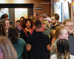 Photo of the crowd in the lobby before the preview performance of The Spitfire Grill in spring of 2024. Young adults are gathered in a small group, excitedly talking and smiling at one another.