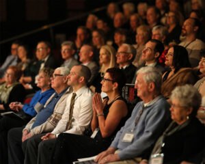 Photo of the audience at our 2024 fundraiser gala. They are watching the stage intently while Dan Murphy, Managing Director, gives a brief speech on the importance of community for the arts to thrive.