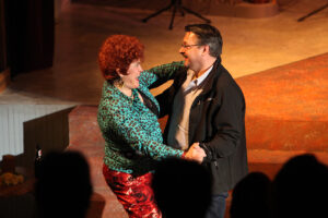 Photo from our 2013 production of Always Patsy Cline with Sharon Maroney as Louise dancing with a member of the audience. She is wearing an outrageous teal leopard print top and a pair of pants with roses printed on them.