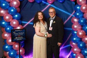 Photo of guests at the prom photo booth at the event. They are in front of a blue and pink balloon arch and blue and pink 1990s themed backdrop.