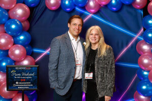 Photo of guests at the prom photo booth at the event. They are in front of a blue and pink balloon arch and blue and pink 1990s themed backdrop.