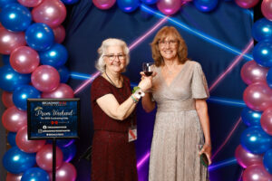 Photo of guests at the prom photo booth at the event. They are in front of a blue and pink balloon arch and blue and pink 1990s themed backdrop.