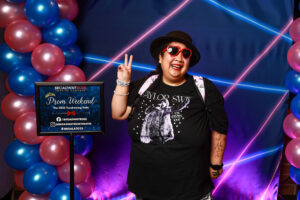 Photo of guests at the prom photo booth at the event. They are in front of a blue and pink balloon arch and blue and pink 1990s themed backdrop.