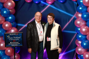 Photo of guests at the prom photo booth at the event. They are in front of a blue and pink balloon arch and blue and pink 1990s themed backdrop.