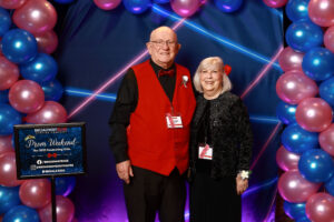 Photo of guests at the prom photo booth at the event. They are in front of a blue and pink balloon arch and blue and pink 1990s themed backdrop.