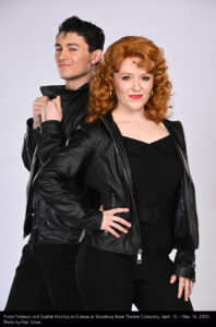 Photo of Victor Polanco and Sophie MacKay in a studio photo session with a gray background. They are in all black outfits like the ones at the end of the show and film version.