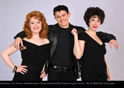 Photo of Sophie MacKay, Victor Polanco, and Melissa Gale in a studio photo session with a gray background. They are in all black outfits like the ones at the end of the show and film version.